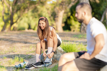 woman putting on inline skates sitting in a park with a man on the side