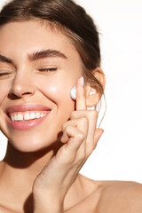 Vertical portrait of smiling happy woman cleansing skin, washing her face with cosmetic facial foam, applying mask, standing over white background