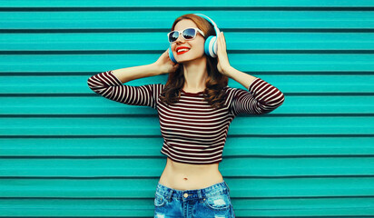 Portrait of happy smiling young woman with headphones listening to music on a colorful blue...