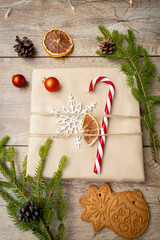Beautiful wrapped gift box with fir branches, candy cane, decor on wooden background. Christmas decorations, New year flat lay, top view flatly, overhead