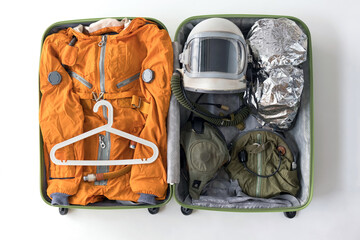 Open suitcase packed for space travelling with orange space suit, space helmet and space suit...