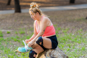 Woman tying her inline skates while sitting on a stone in a park