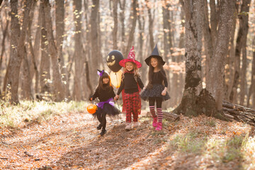 three little girls in witch costumes laugh, conjure, walk through the autumn forest with baskets for sweets in the shape of pumpkins. halloween concept, lifestyle . High quality photo