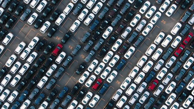 Long rows of finished white black red and blue automobiles on open warehouse parking lot of car factory giant aerial view