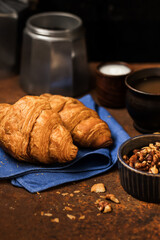 French breakfast. Freshly baked croissants, a cup of coffee, jam and nuts on an aged rusty background. Dark style still life concept with copy space. 