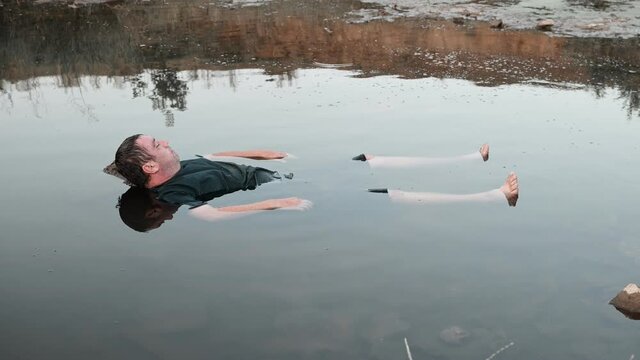 a man drowned , dead in the water , the body of a young man aged lies in the lake facing up, a corpse in a dirty pond unstable camera movement color correction.