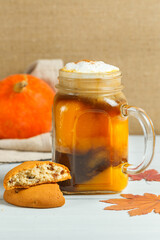 Glass mug with Pumpkin latte and cookies close-up on a black background, vertically with space. Hot seasonal drink