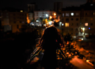 Silhouette of a female face on a light background. SIlhouette of a lonely doll with long hair at night with backlight of city view from window