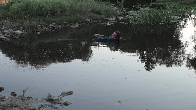 a man drowned , dead in the water , the body of a young man aged lies in the lake with his head on a stone, a corpse in a dirty pond unstable camera movement color correction.