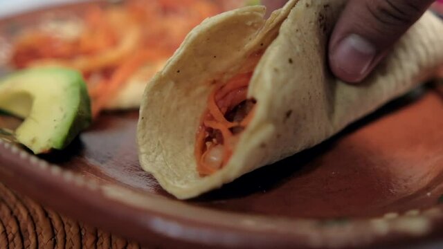 Hand holding vegan Mexican tinga tacos on traditional clay plate