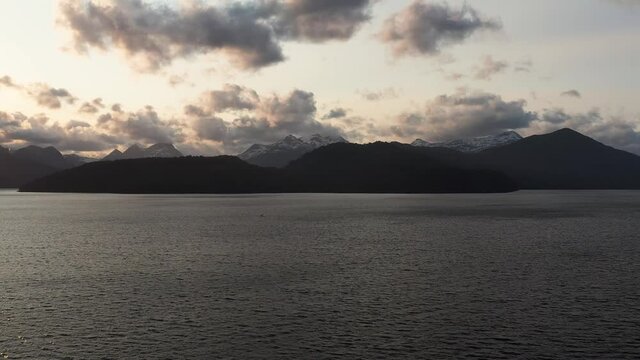 Aerial panning shot of Andes Mountain range across Lake Nahuel Huapi from the town of Villa La Angustura at sunset with side lit clouds