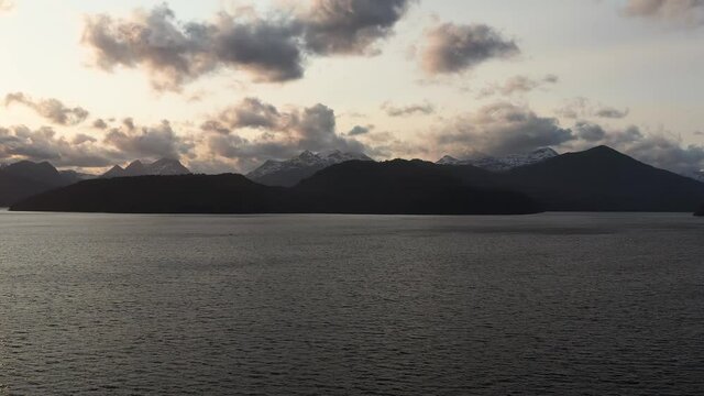 Aerial zoom shot of Andes Mountain range across Lake Nahuel Huapi from the town of Villa La Angustura at sunset with side lit clouds