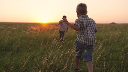 Happy children, boys run together in park at sunset on grass. People in park joyful jogging. Happy family, sons are running on field in rays of sun. Child, toddlers have fun playing outdoors in summer