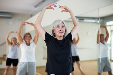Interested aged woman practicing ballet dance moves during group class in choreographic studio.