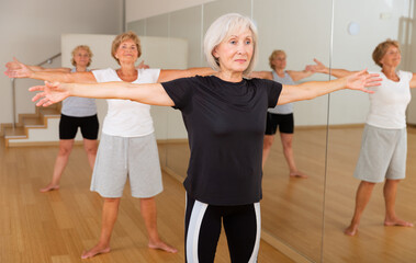 Fototapeta premium Sporty mature woman practicing Hatha yoga with group of females in modern fitness studio, making stretching and relaxing exercises.