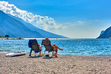 Torbole, Italy-09 October 2018: People sitting at the beach on the lounge chair and admiring Lake...
