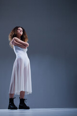 Beautiful girl with curly hair. Ballerina in white dress and black boots.