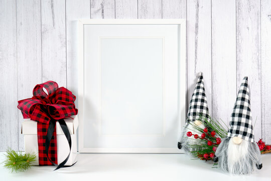 Vertical wall art print frame product mockup. Christmas farmhouse theme SVG craft product mockup styled with gift with buffalo plaid bow and farmhouse style gnomes against a white wood background.