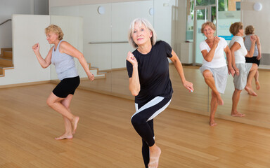 Fototapeta na wymiar Positive aged woman practicing vigorous dance movements in group dance class .