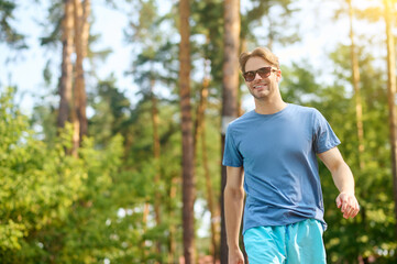 Naklejka na ściany i meble A young man in a blue tshirt and sunglasses near swimming pool