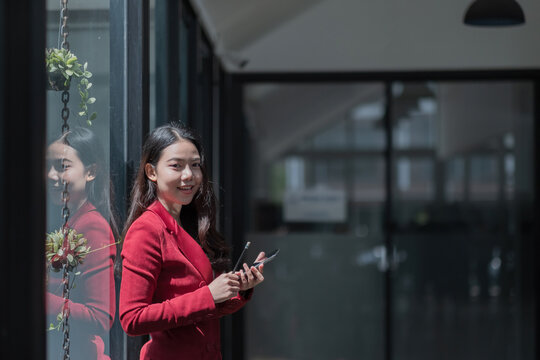 Image of young asian woman holding mobile phone while working in office, she looking at camera