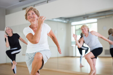Fototapeta premium Portrait of mature energetic woman and people practicing active dancing in the studio at a group lesson