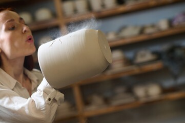 A female potter blowing on a newlymade pot