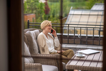 Obraz premium Pleased middle-aged lady talking on the smartphone outdoors