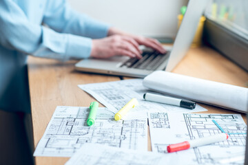 Construction plan on windowsill and female hands near laptop