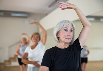 Aged women performing ballet dance during their group training in fitness room.