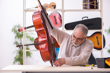 Old male repairman repairing musical instruments at workplace