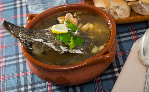 Delicious fish broth with sturgeon served in clayware with greens and lemon slice..
