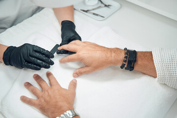 Professional manicurist filing man nails with emery board