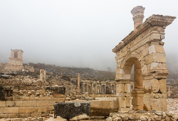 Fototapeta na wymiar Remained honorific arched gate and Corinthian column at important Turkish archaeological site of Sagalassos on misty winter day