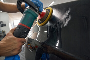Car detailing studio worker polishing car varnish with electric polisher