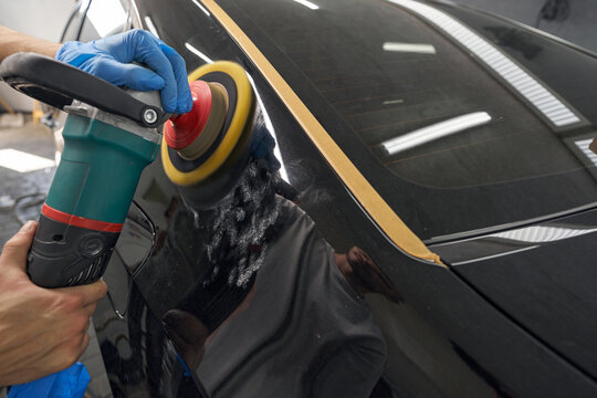 Auto mechanic worker polishing car body at automobile repair station shop by power buffer machine
