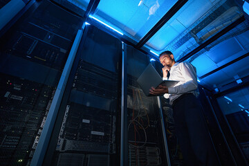 IT technician analyzing data from laptop in server room - Powered by Adobe