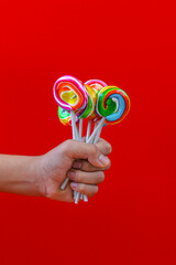 Close-up of hands holding colorful lollipops on red background 