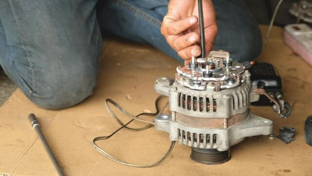 The mechanic is unscrewing the assembly of the dynamo