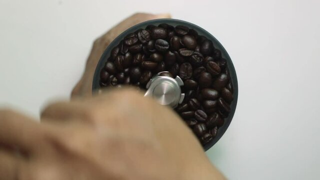 A man's hands grinding roasted coffee beans with a hand crank coffee grinder.