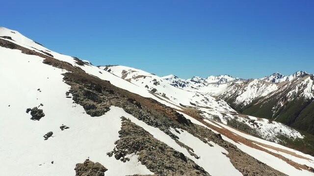 Aerial ascending drone shot of ski slopes and mountain range in melt in spring at the Cerro Bayo ski resort near Villa La Angostura, revealing forest and distant mountain range