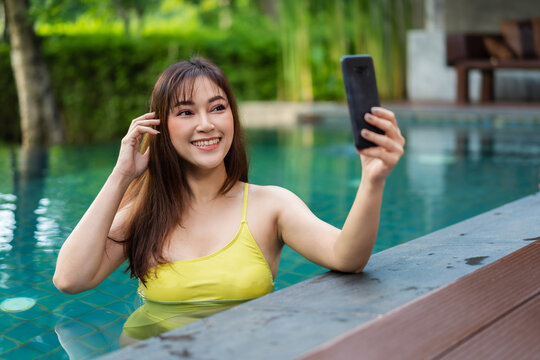 happy woman using smartphone to selfie a photo in swimming pool