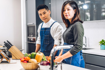 Young asian family couple having fun cooking together with fresh vegetable healthy food clean on table.Happy couple prepare the food yummy eating lunch in kitchen