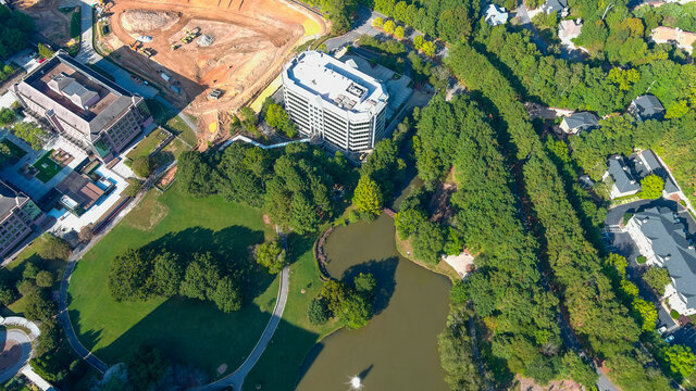 a majestic aerial shot of a water fountain in the middle of a lush green lake surrounded by lush green and autumn colored trees at Lenox Park in Brookhaven Georgia USA