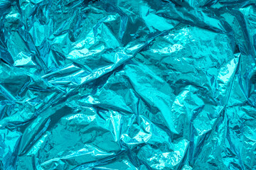 Aqua blue crumpled, creased iridescent metal foil texture. Abstract colored background. Shiny monochrome surface.
