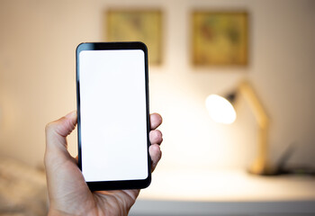 Hand holding smartphone with blank screen. Using smartphone indoors.