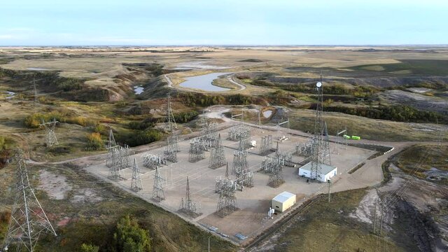 4k backwards flight over electricity masts and power lines in vast prairie setting. Warm colours during golden hour. Generating station in rural Alberta, Canada.