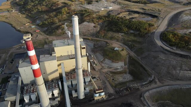 Slow 4k sideways flight over gas and coal power plant in rural Country setting during sunset. High resolution aerial footage.