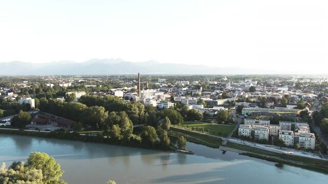 Aerial shot of a skyline starting with a industrial area,
ending at the residential buildings showing them both
together in frame, in the distance are the
mountains, in the front is a river and trees.