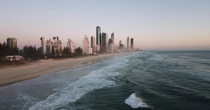 Drone pan over a beach city with waves during sunrise